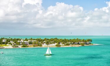 Un voilier passe devant une île tropicale, parfaite pour la Floride en famille, sous un ciel nuageux.