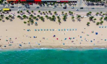 Vue aérienne d'une plage de sable de la Floride en famille, avec des parasols, des gens et de l'eau turquoise.